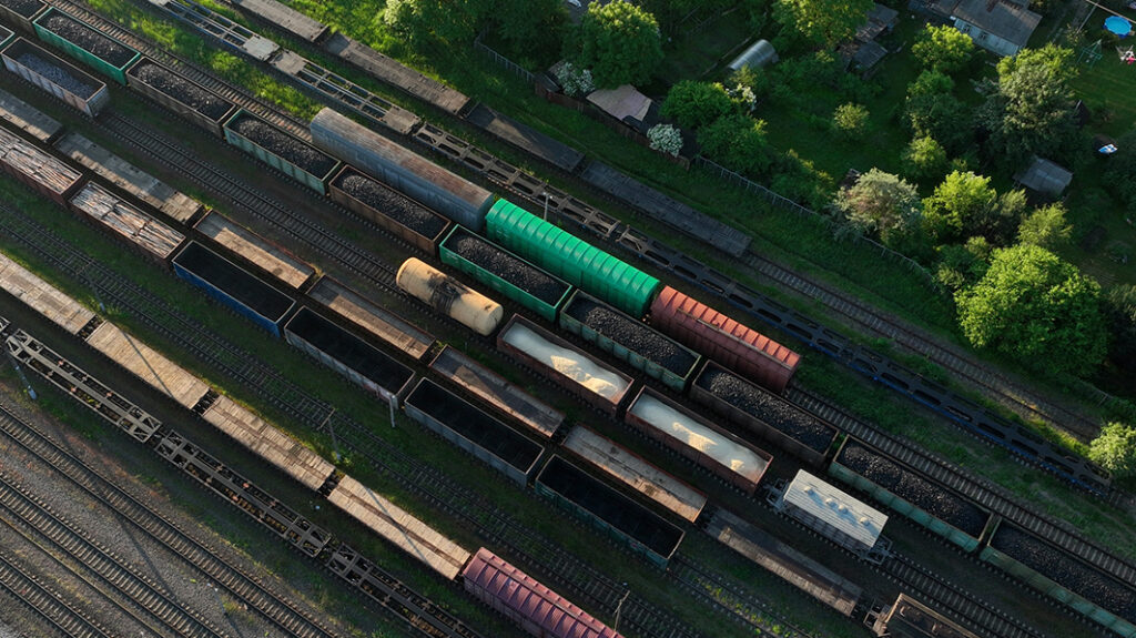 Aerial view of a railway yard with various colorful freight cars parked on multiple tracks, surrounded by lush greenery