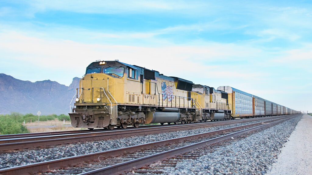 Long freight train with yellow locomotives passing through a desert area with distant mountains under a clear sky