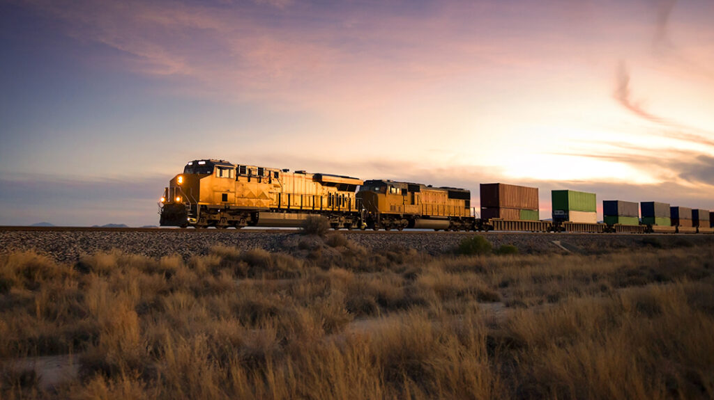 Freight train hauling containers across a desert landscape at dusk, highlighting the vastness of rail transport