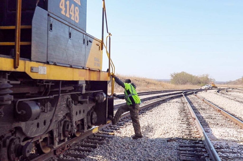 Railroad worker in high visibility vest manually operating track switch next to a locomotive
