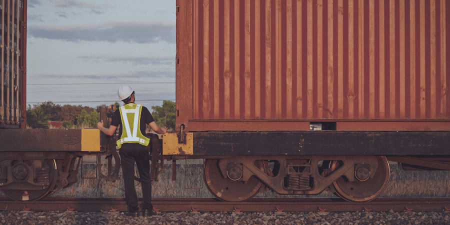 Railroad worker inspecting a red freight container on a train carriage at dusk